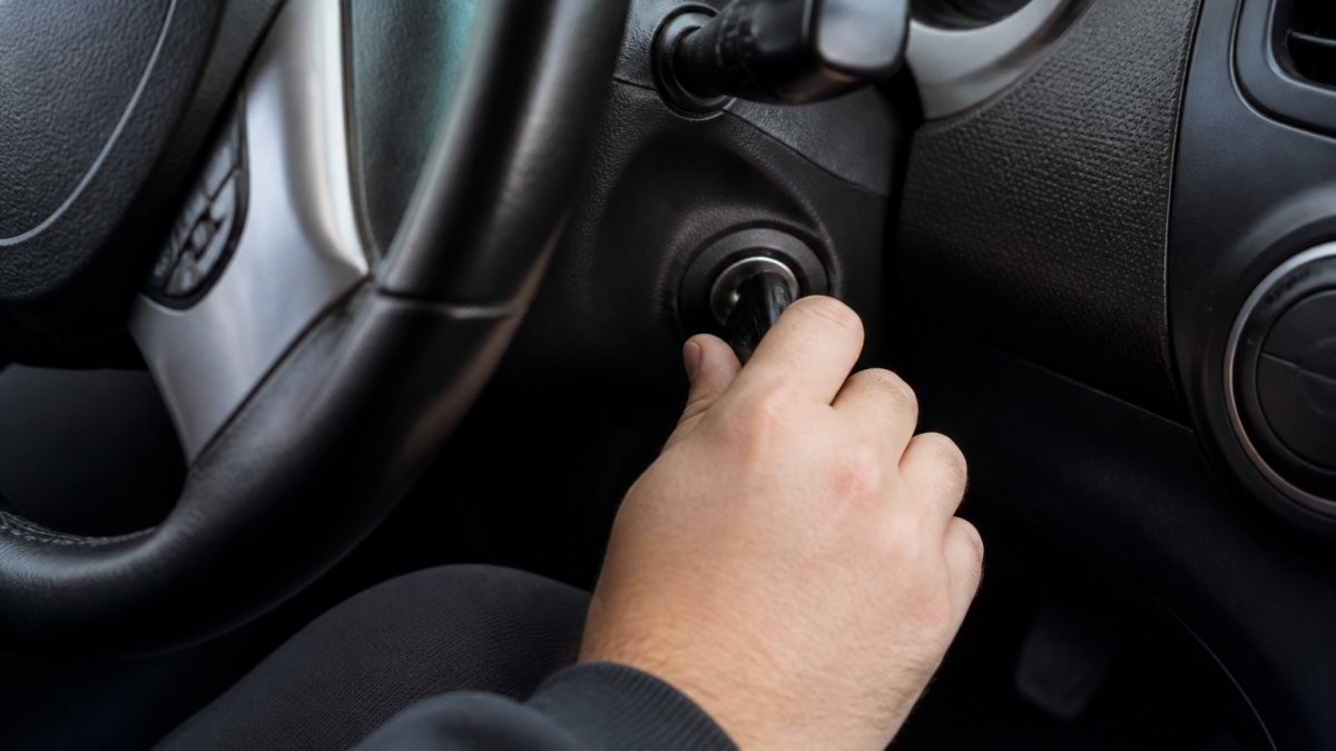 Close-up of a driver's hand turning the ignition key through different positions (off, on, off) inside a vehicle, showing the steering wheel and dashboard
